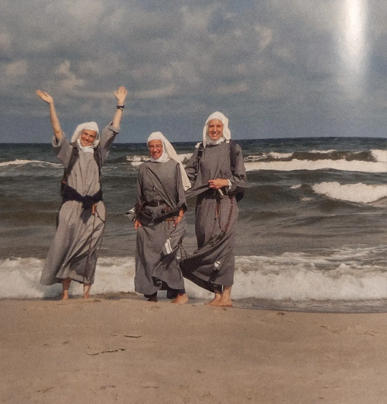 Three sisters laughing on a beach with their arms in the air.